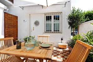 Una mesa de madera con sillas, suelo de cuadros, una puerta blanca, una ventana con barrotes y una planta pequeña.