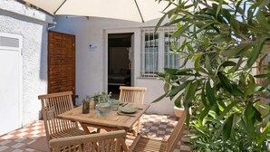 Eine Außenpatio mit Holztisch und -stühlen, einer weißen Wand, einer Holztür und einem Fenster mit weißen Gitterstäben.