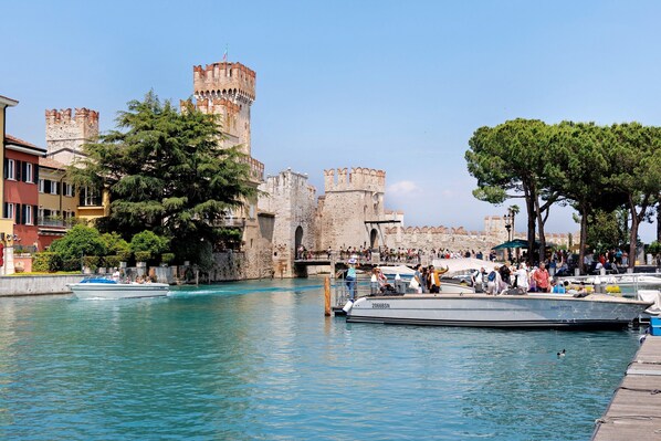 A historic castle with towers, a waterfront with boats, and a crowd of people.
