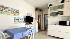 Un comedor con mantel azul, sillas blancas, televisión y obras de arte en la pared.