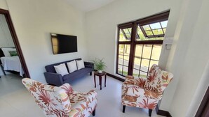 Ein Wohnzimmer mit einer Couch, zwei Sesseln, einem Couchtisch und einem Fernseher an der Wand.