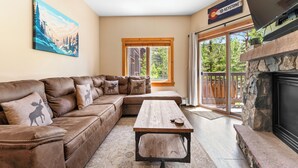 A living room with a brown leather sectional sofa, a wooden coffee table, a fireplace, and a large window with a view of trees. - Expedition Station lodge at River Run Village, steps to gondola, pool, and gym

 (Keystone)