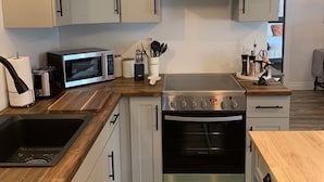 Una cocina moderna con armarios blancos, campana extractora de acero inoxidable, microondas, tostadora y lavavajillas.