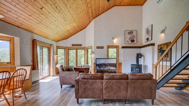 Ein geräumiges Wohnzimmer mit Holzboden, einem großen Fernseher, einem Kamin und einer Treppe.