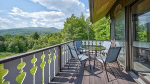 Ein Balkon mit Glasgeländer, Gartenmöbeln und Blick auf eine bewaldete Landschaft.