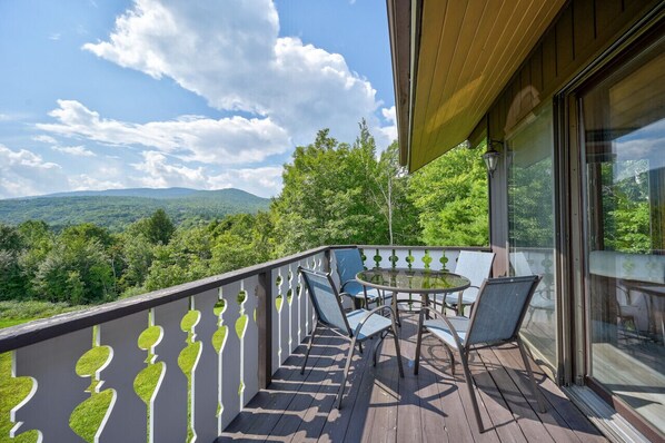 Un balcon doté d’une balustrade en verre, de mobilier d’extérieur et offrant une vue sur un paysage boisé.