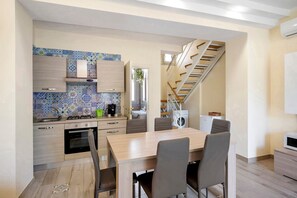 Une cuisine moderne avec un coin repas, des meubles en bois, un pare-feu en carreaux et un escalier menant à l’étage supérieur.