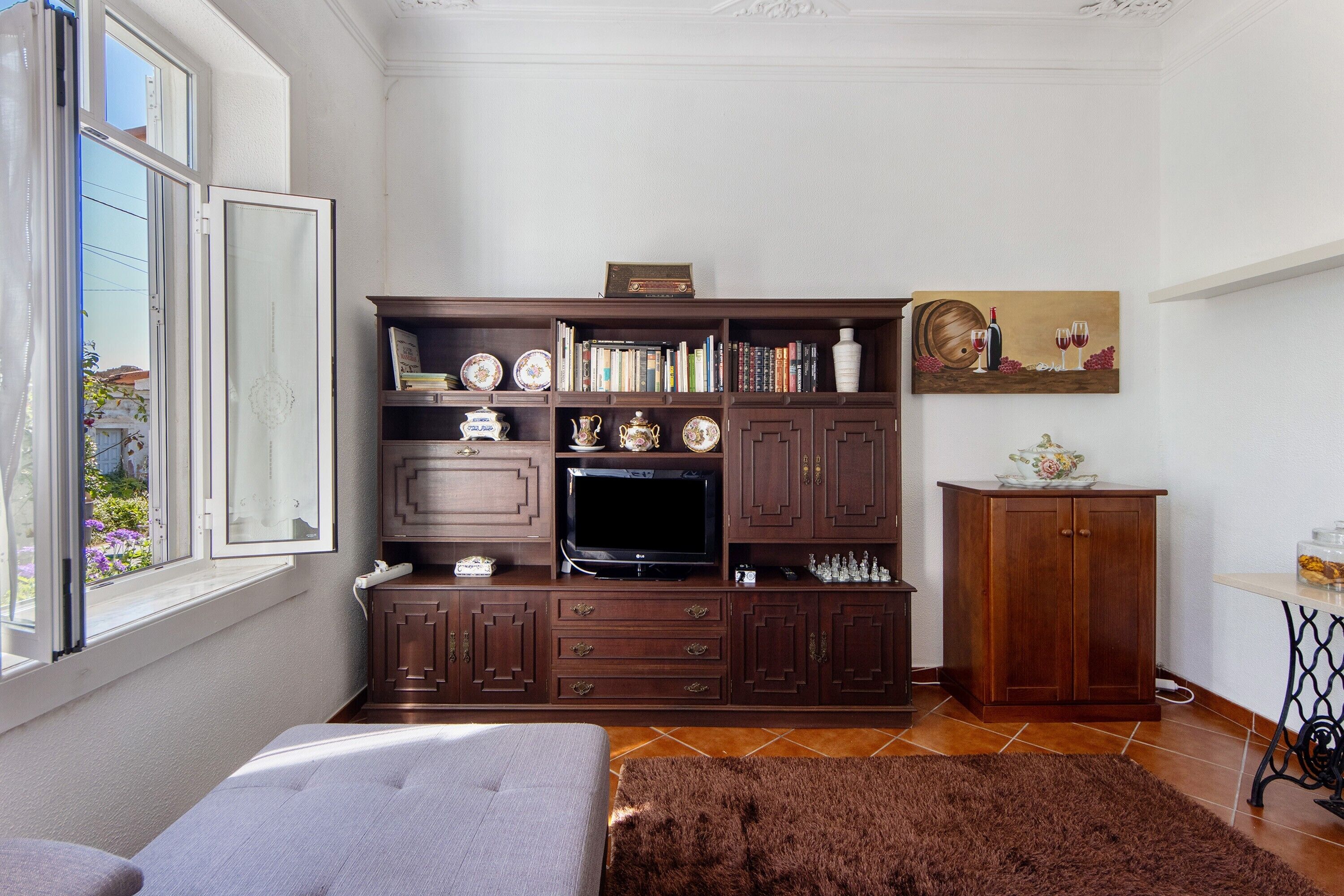 A room with a bed, a TV, wooden cabinets, a window, and a painting.
