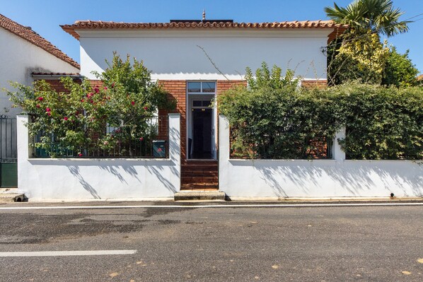 A two-story building with a white facade, a tiled roof, and a wooden entrance door.