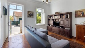 Un soggiorno con divano, televisione, mobiletto in legno e una porta che dà sull'esterno.