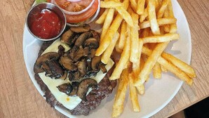Un plato con una hamburguesa, champiñones, papas fritas, una ensalada y una bebida.