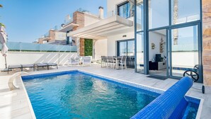 Un'area piscina moderna con piscina cristallina, lettini prendisole e veranda vetrata.