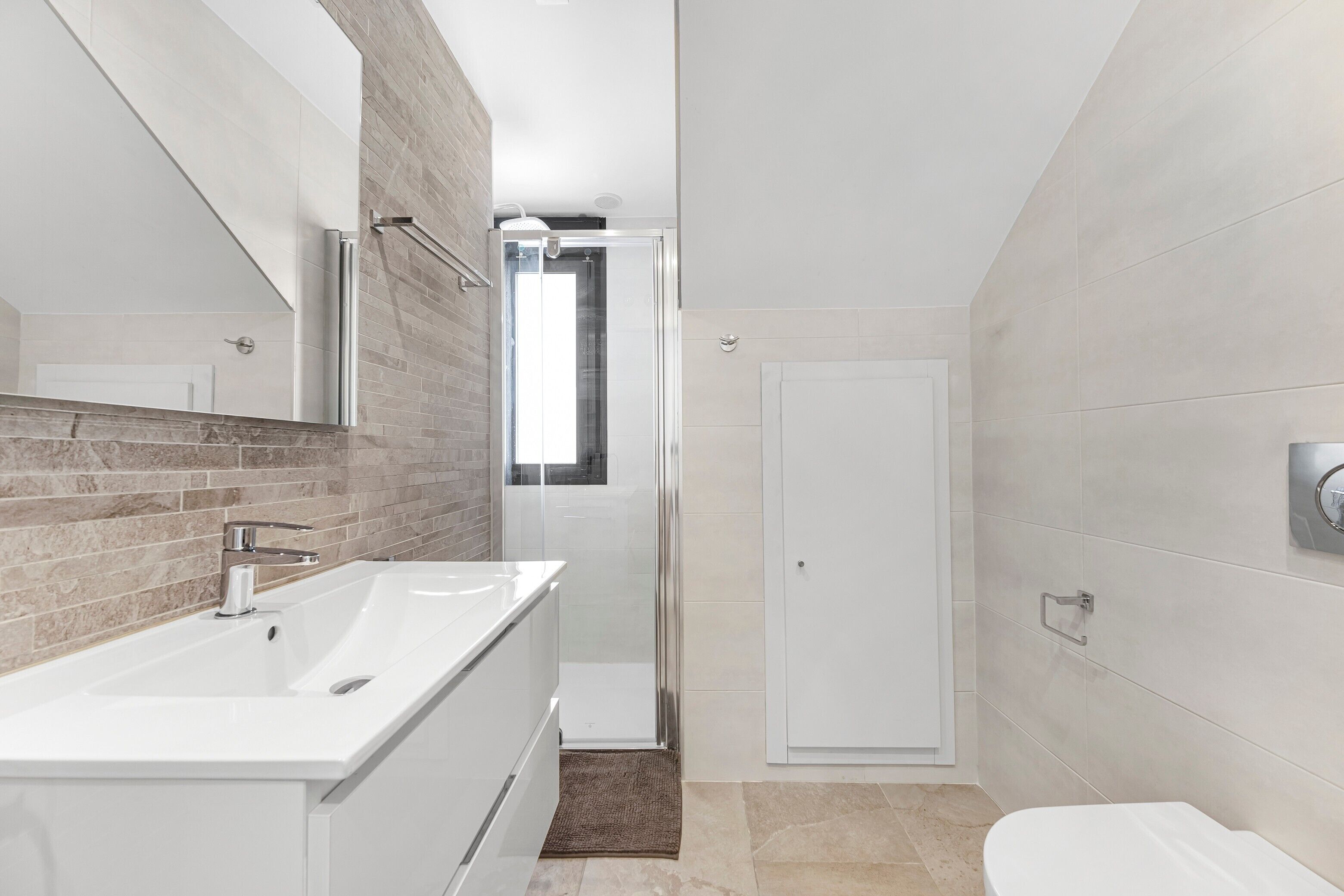 A modern bathroom with a large mirror, a white sink, a shower, and a toilet.