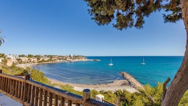 Vista sulla costa con ringhiera in legno, mare blu limpido e una piccola isola con edifici.