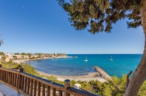 Vista costera con barandilla de madera, mar azul cristalino y una pequeña isla con edificios.