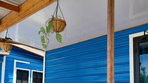 Una terraza de madera con barandilla, una planta colgante y una pared exterior azul.