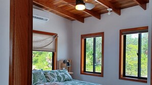 Un dormitorio con cama, vigas de madera en el techo y ventanas que dan a zonas verdes.