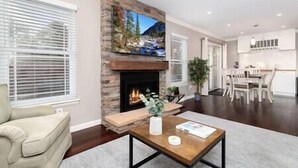 A living room with a stone fireplace, a television mounted above it, and a dining area with a table and chairs. - Charming Arvada Home, Community Pool Jun-Aug (Arvada)