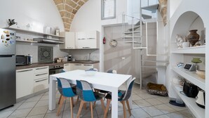 A compact kitchen with white cabinetry, a dining table with chairs, a small dog bed, and a staircase leading to an upper level.