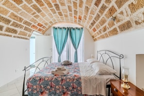 A bedroom with a brick ceiling, a bed with floral bedding, a bedside table with a lamp, and a window with curtains. - Holiday Home 'Civico4 Luxuryholidays' with Private Terrace, Wi-Fi and Air Conditioning (Casarano)