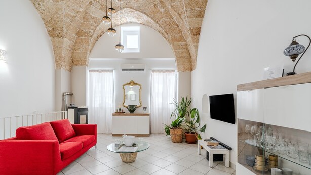 A living room with a red sofa, a glass coffee table, a white cabinet, and a TV mounted on the wall.