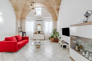 Una sala de estar con un sofá rojo, una mesa de centro de vidrio, un mueble blanco y un televisor montado en la pared.