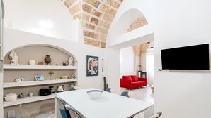 A dining area with a white table, blue chairs, and a white shelf with kitchen items.