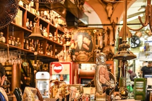Interno di un negozio disordinato, con numerosi articoli sugli scaffali e appesi, tra cui una campana, una statua e un frigorifero Coca-Cola.