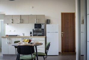 A compact kitchen with a microwave, toaster, and refrigerator. There is a dining table with chairs and a bowl of fruit.