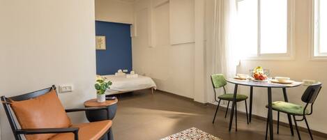 Una habitación de hotel con cama, una pequeña mesa con sillas, ventana con cortinas y ventilador de techo.