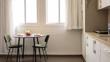 Un comedor con una mesa dispuesta para dos, sillas, una ventana con cortinas y una encimera de cocina con armarios.