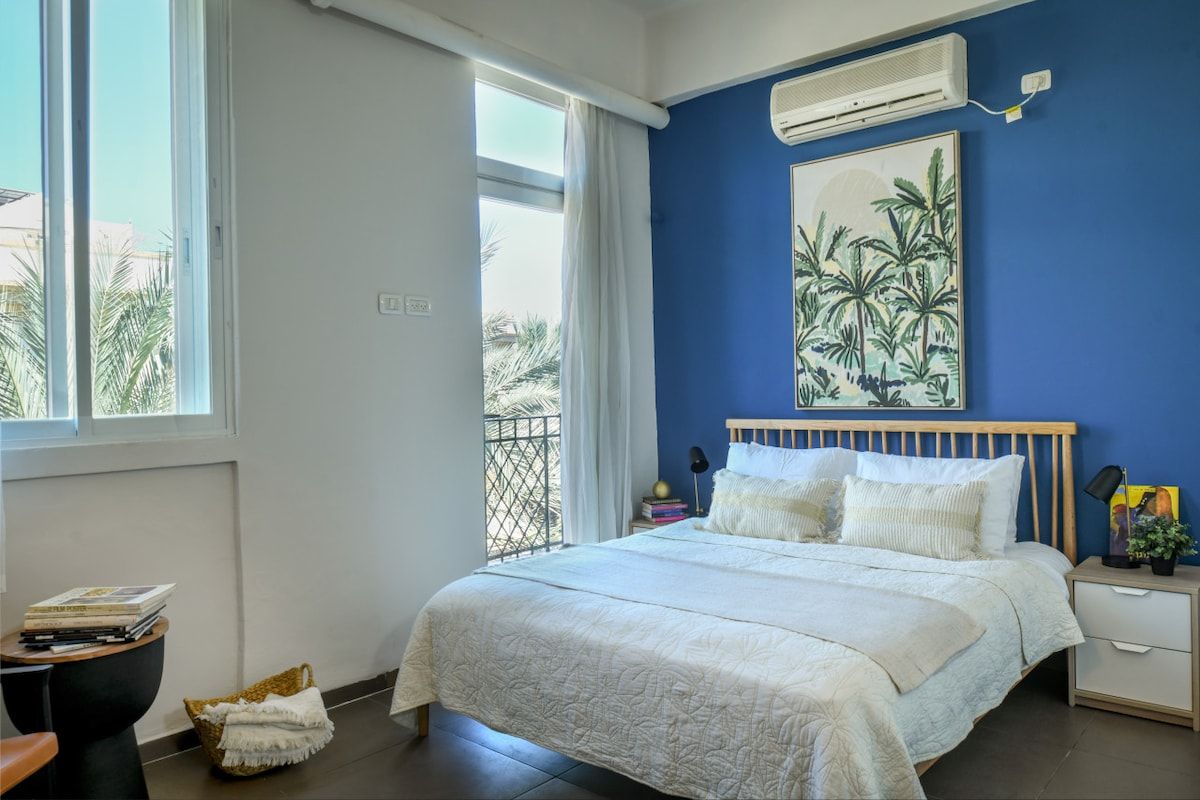 Une chambre à coucher comprenant un lit, une table de chevet, une lampe, une fenêtre et un appareil de climatisation.
