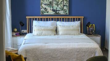 Un dormitorio con cama, mesita de noche, lámpara y una obra de arte en la pared.