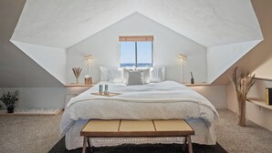 Een slaapkamer met een schuine kap, een groot bed, bedlampen, een raam en een nachtkastje met dienblad.