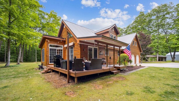 Una cabaña de troncos con terraza, asientos exteriores y una bandera estadounidense.