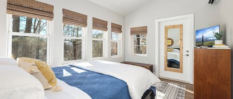 A bedroom with a bed, a ceiling fan, a TV, and a window with a view of trees.