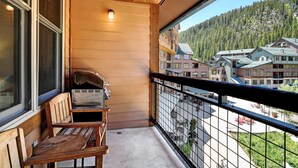 A balcony with a grill, wooden bench, and a view of a mountain village. - WP Resort Ski In Out Condo 2403 I Hot Tub I Gym I Ski Views I Bunk Room I Discounted Attractions (Winter Park)