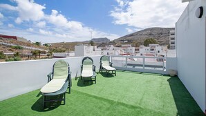 A rooftop terrace with artificial grass, two lounge chairs, and a view of a mountainous landscape.