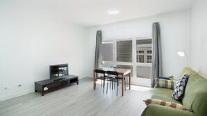 A modern living room with a flat-screen TV, a dining table with chairs, a sofa, and a window with curtains.