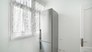 A white room with a stainless steel refrigerator, a window with floral curtains, and a closed door.