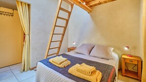 Ein Schlafzimmer mit einem Bett, einer Holzleiter, einem Nachttisch mit Lampe und einer Tür mit Vorhängen.