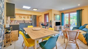 Eine moderne Küche mit Essbereich, ein Wohnzimmer mit Sofa und Fernseher sowie ein Balkon mit Vorhängen.