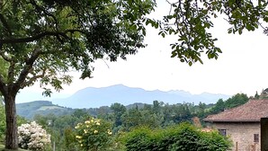 Ländliche Landschaft mit einem Haus, Bäumen und Bergen im Hintergrund.