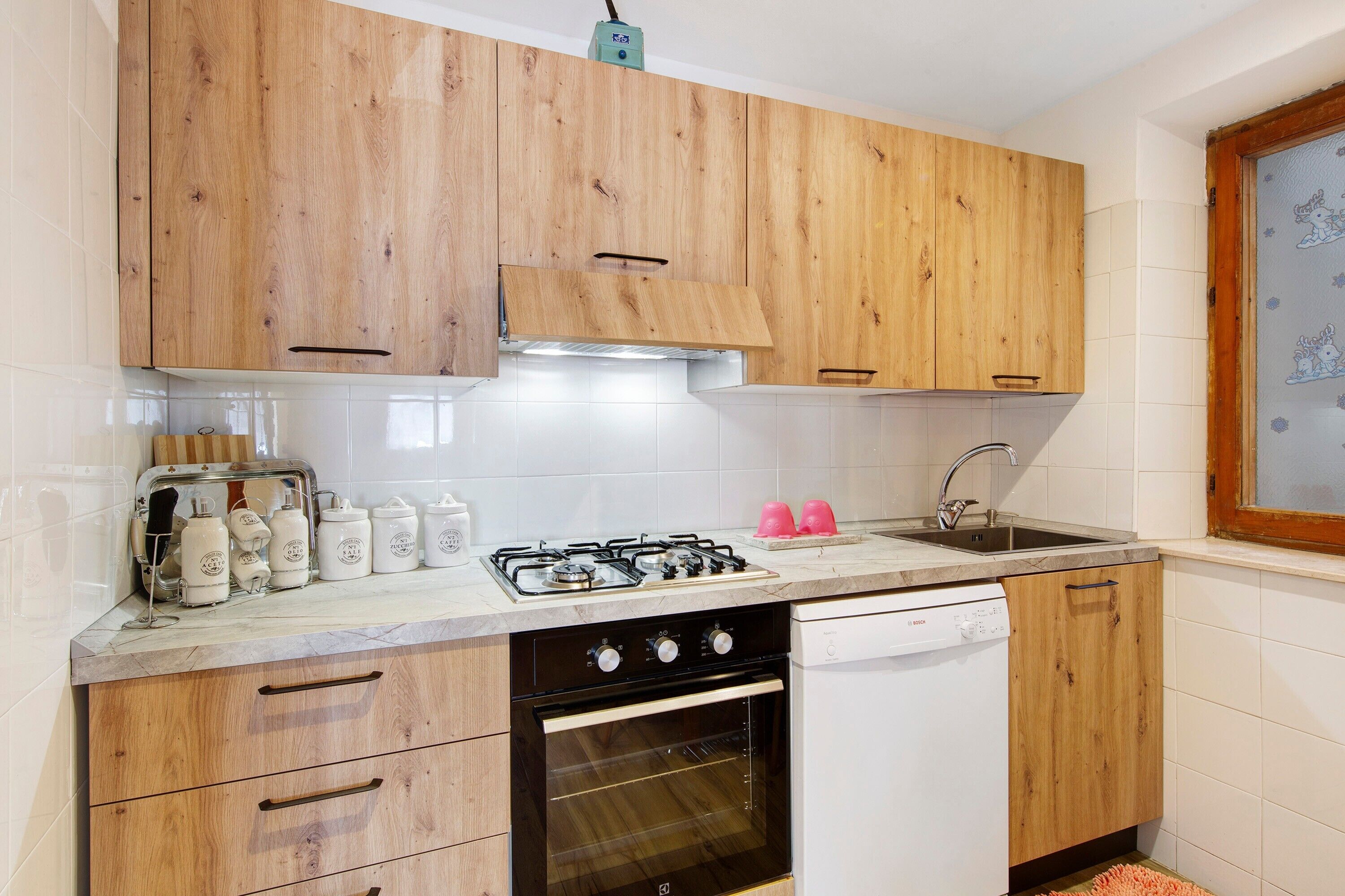 Una cocina con armarios de madera, estufa a gas, lavavajillas y ventana con vistas.