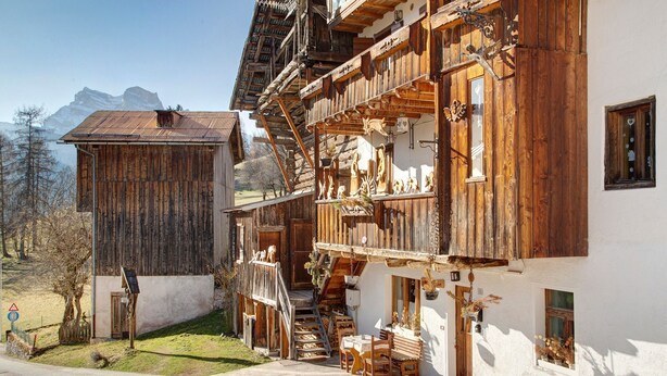 Ein traditionelles Holzhaus mit Balkon, Treppe und kleinem Tisch vor der Tür.