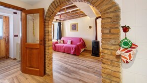 Ein Zimmer mit Holztür, Ziegelbogen, rotem Sofa, Heizkörper und einer an der Wand befestigten Obstschale.