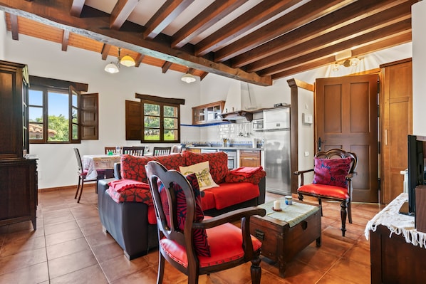 A spacious living area with a wooden ceiling, a sofa set, a dining table, and a kitchen area with a refrigerator.