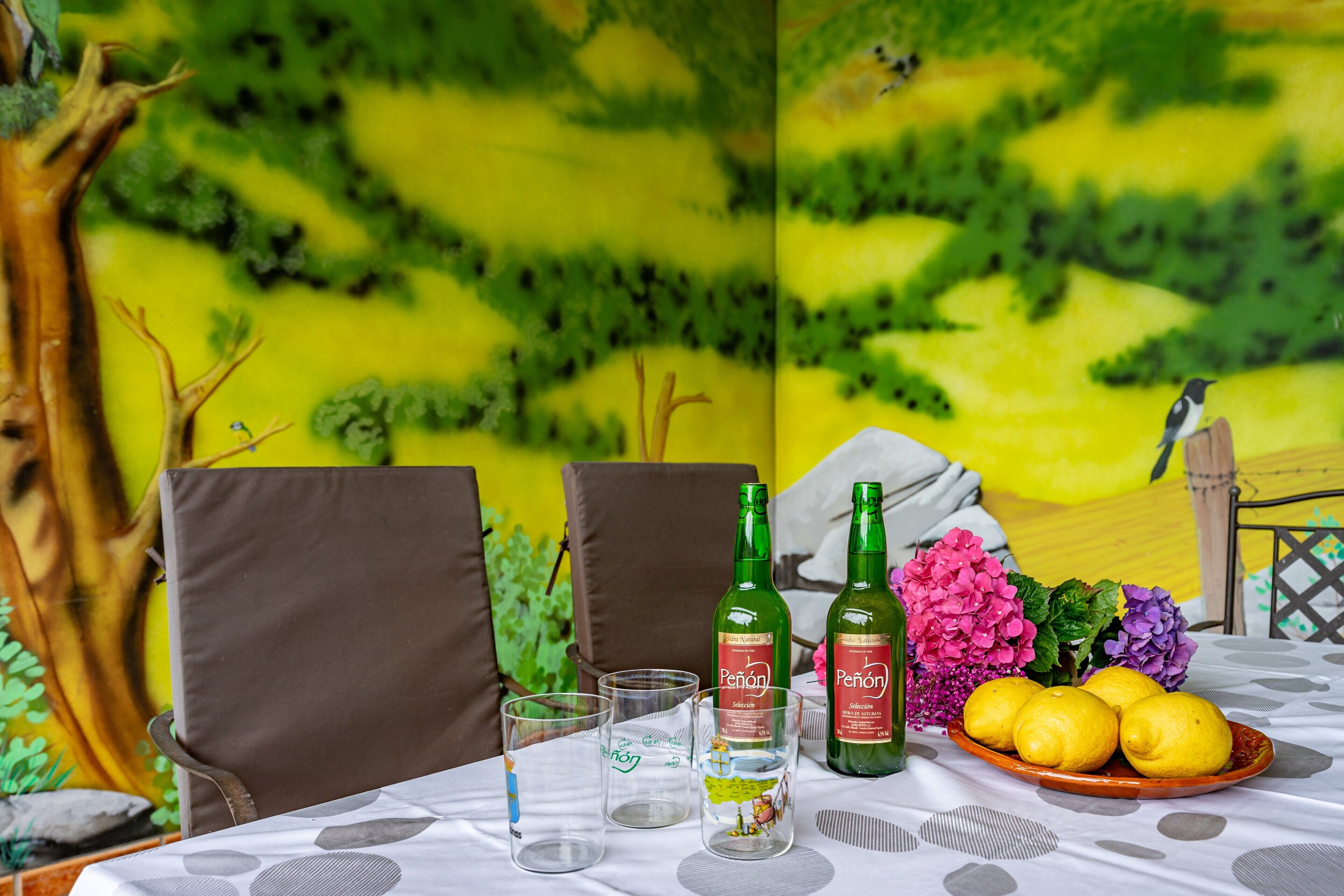 Ein Esstisch mit zwei Stühlen, zwei Gläsern, zwei Flaschen Penonil Wein, einer Zitronenplatte und einer Vase mit Blumen.