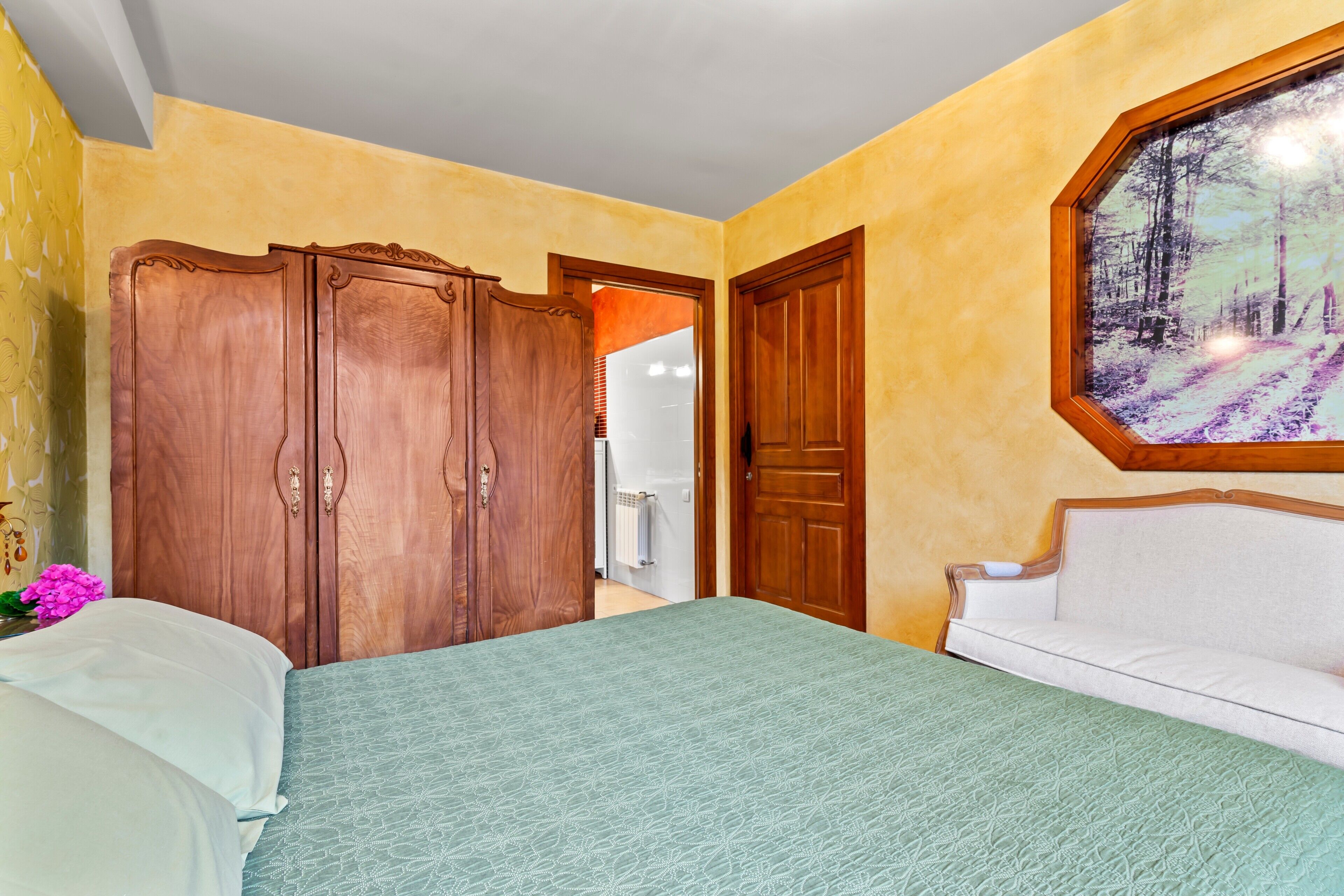 A bedroom with a bed, a wardrobe, a sofa, and a painting on the wall.