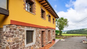 A yellow building with stone and brick exterior, a paved driveway, and a view of green hills. - Apartment 'La Llosa' with Mountain Views, Private Terrace and Wi-Fi (Logrezana)